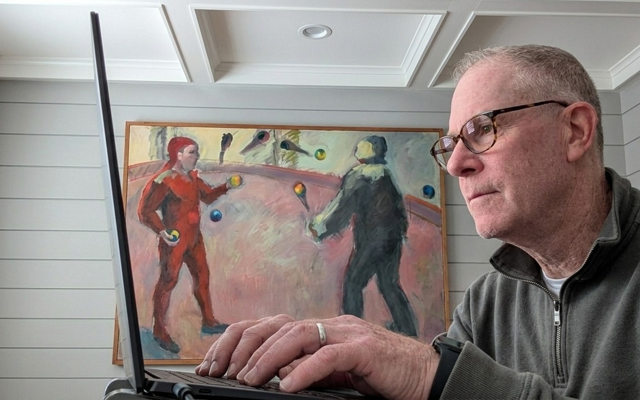Fred Skoler working on a laptop, a painting of jugglers behind him