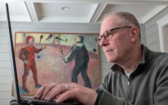 Fred Skoler working on a laptop, a painting of jugglers behind him